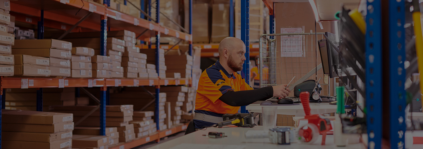 Man sat working at bench in busy warehouse